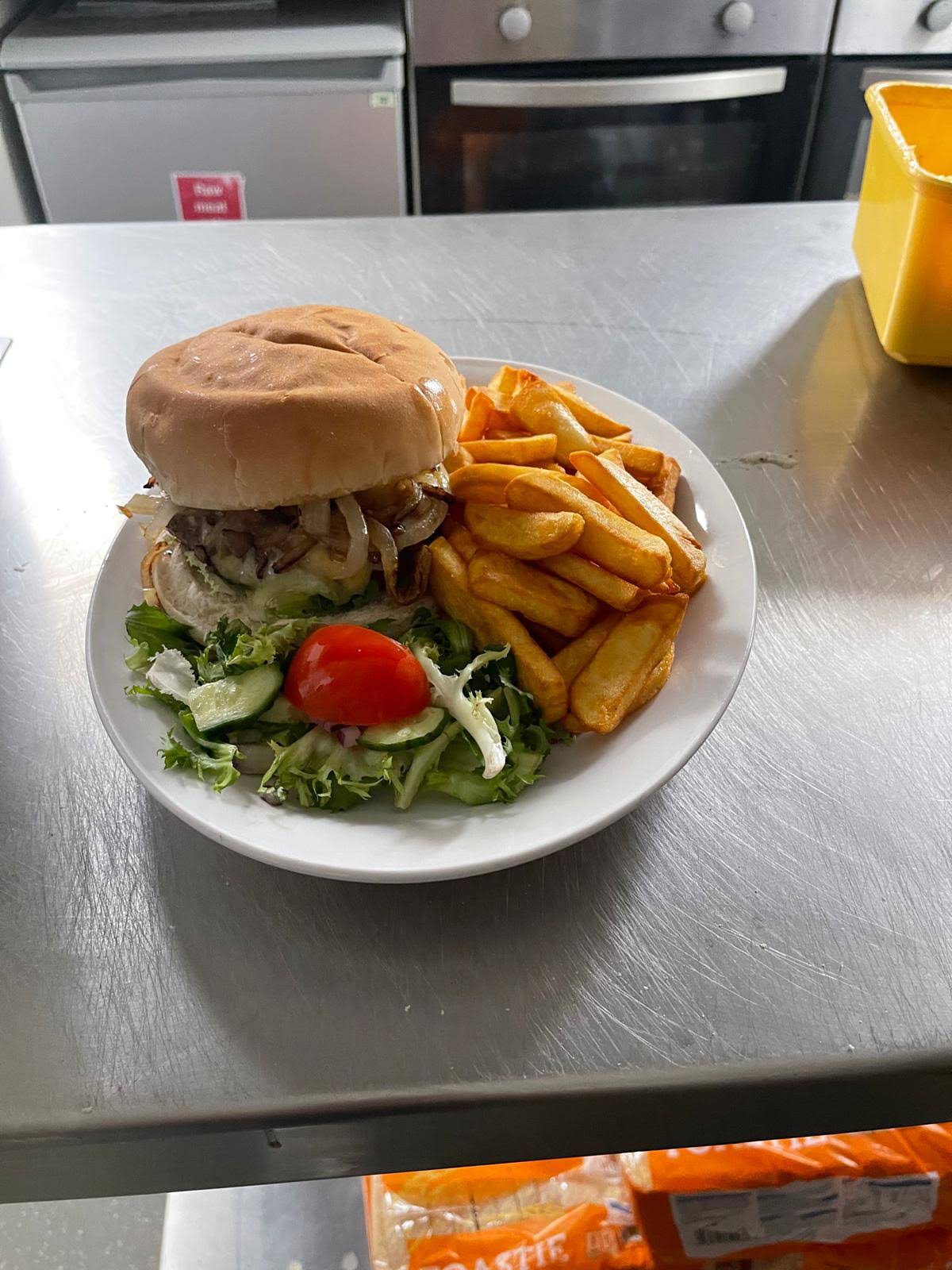 A burger, chips and salad on a white plate in the café kitchen